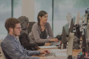 A group of people sitting at computers in front of windows.