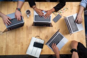 A group of people sitting around laptops on top of a table.